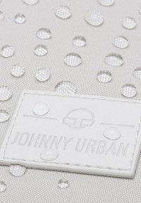 A vízálló anyag világosszürke árnyalatban, kiemelkedő vízcseppekkel rendelkezik. Egy fehér, dombornyomott címke látható, rajta a "JOHNNY URBAN" felirattal, amely hangsúlyozza a márkát.