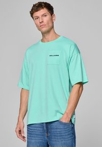 Miętowa, oversize'owa koszulka z krótkim rękawem, z kieszonką na piersi oraz nadrukiem "WILLIAMS" w kolorze czarnym. Wykonana z miękkiej bawełny, o luźnym kroju.