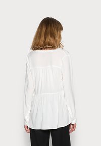 Blusa branca de manga longa com decote redondo, design com costas franzidas e punhos abotoados, feita de um tecido leve e suave.