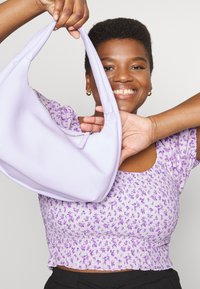 Bolsa de ombro em pele roxa com um design arredondado e um detalhe de fecho. Parte superior texturizada com padrão floral em tons de roxo.