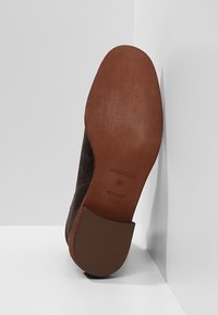 Bruna mockaskinnskor med en slät rund tå och en platt gummisula. Har en detaljerad textur och subtil branding på sulan.