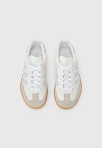 Λευκά και γκρι αθλητικά παπούτσια με ανοιχτό μπλε λεπτομέρειες, με τρεις ρίγες, σουέτ μύτη και σόλα από καουτσούκ χρώματος τσίχλας.