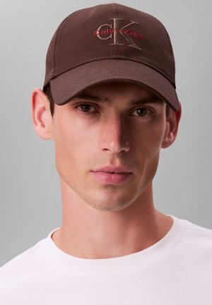 Braune Baumwoll-Baseballkappe mit gesticktem "Calvin Klein"-Logo in Rot und "CK" in einer helleren Farbe. Gebogener Schirm und genähte Akzente.