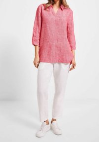 Roze linnen tuniek met een V-hals en driekwartmouwen, gedragen met witte linnen broek en witte sneakers. Glad textuur, ontspannen pasvorm.