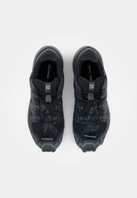 Schwarze Sportschuhe mit einem strukturierten Mesh-Obermaterial, ausgestattet mit einem Schnürsystem und einem auffälligen Logo auf der Zunge. Strapazierfähige Gummisohle mit Grip-Mustern.