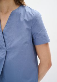 Maglietta in cotone blu con scollatura a V, maniche corte arrotolate e una vestibilità leggermente rilassata. Presenta una texture sottile e un design minimal.
