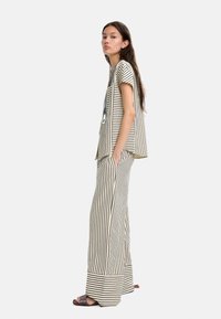 Completo a righe composto da una maglietta a maniche corte e pantaloni a gamba larga in beige e nero. Progettato con una vestibilità ampia e tasche laterali.