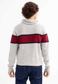 Suéter de punto gris con cuello de tipo cowl, que presenta un patrón de rayas horizontales en rojo y negro. Puños acanalados y vista trasera mostrada.