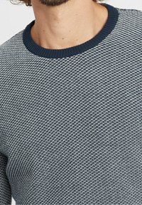 Marinblå och vit mönstrad stickad tröja med ribbad rund halsringning. Texturen har en vävd design, synliga stygn och avslappnad passform.