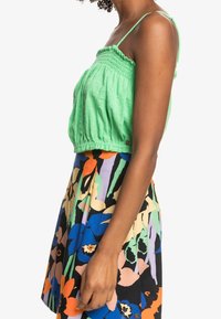Vihreä lyhyt toppi joustavalla smokkikujalla, yhdistettynä eloisasti kukkakuosiseksi hameeksi, jossa on sinisiä, oransseja ja vihreitä sävyjä.