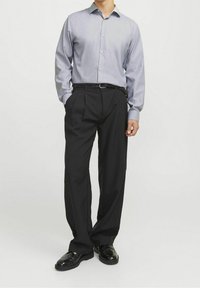 Camicia grigia chiara a maniche lunghe, pantaloni neri plissettati, cintura intrecciata, scarpe nere lucide. La camicia presenta un colletto e una chiusura con bottoni.