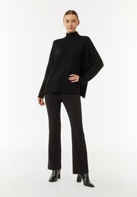 Czarny sweter z golfem wykonany z dzianiny, o luźnym kroju, w połączeniu z czarnymi spodniami dzwonami oraz czółenkami na obcasie. Prosty, elegancki design.