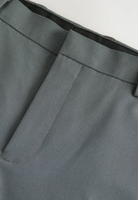 Pantalones grises con una textura suave, que presentan una cinturilla ancha, costuras cuidadas y un diseño frontal plano.