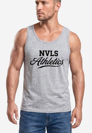 Muscular man wearing a gray sleeveless shirt with "NVLS Athletics" printed in black, paired with blue jeans, looking to his left.