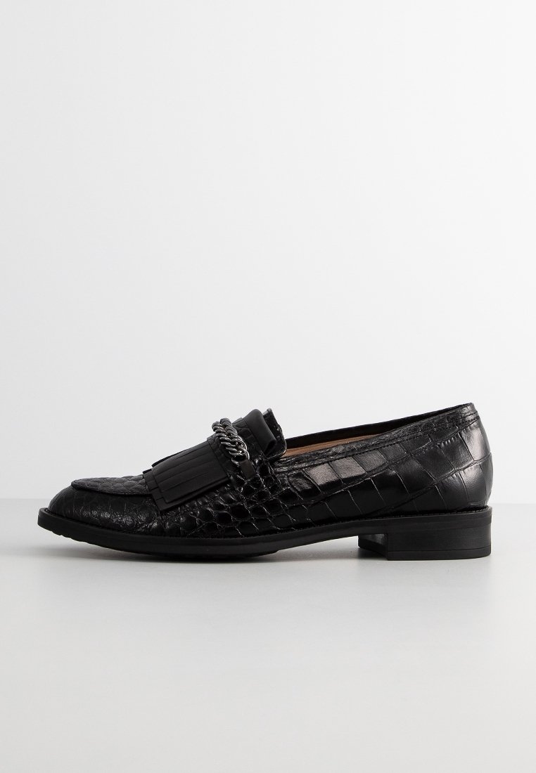 Mocassin en cuir noir avec texture crocodile, frange décorative et détail en chaîne argentée, talon plat, vue latérale sur fond blanc.