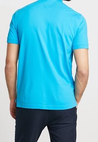 Koszulka polo z krótkim rękawem w jasnym turkusowym kolorze, wykonana z gładkiej bawełny, z klasycznym kołnierzykiem, pokazana od tyłu z dopasowanym krojem.