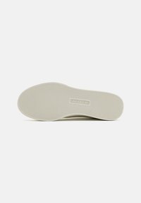Sola do sapato Skechers em borracha bege claro, apresentando uma superfície texturizada com ranhuras horizontais e verticais. Logotipo visível na lateral.