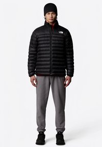 Juoda pūkinė striukė su horizontaliomis siūlėmis ir aukštu apykakliu, derinama su pilkomis sportinėmis kelnėmis ir juodais sportiniais batais. Paprastas dizainas.