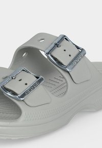 Ανοιχτό γκρι σανδάλι Crocs με δύο ρυθμιζόμενες ασημένιες αγκράφες και υφασμένο πέλμα για άνεση και κράτημα.