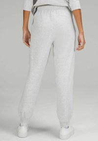 Graue Sweatpants mit entspannter Passform, elastischem Bund und schmal zulaufenden Knöcheln, aus weichem Material, kombiniert mit weißen Sneakers.