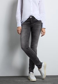 Grå smala jeans med en blekt textur, kombinerat med en vit långärmad tröja och vita sneakers. Outfiten är modern och avslappnad.