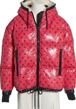 Chaqueta acolchada roja brillante con patrón floral en blanco y negro, cremallera negra, capucha con cordón y puños negros en un maniquí.