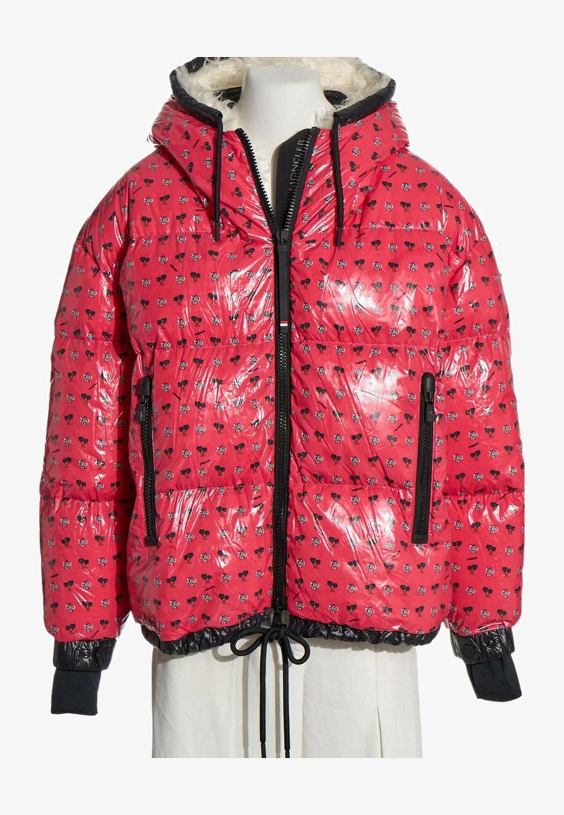Doudoune rouge brillante avec motif floral noir et blanc, fermeture éclair noire, capuche à cordon et poignets noirs sur un mannequin.