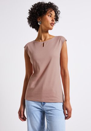 Beige fitted top with short cap sleeves and a small keyhole detail at the neckline. Smooth texture, paired with light blue denim jeans.