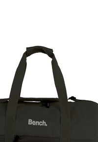 Donkergrijze duffeltas met stoffen bandjes en een gestructureerde afwerking. Heeft een zichtbare rits en het "Bench."-logo aan de voorkant.