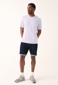 Vaalean violetti lyhythihainen t-paita, tummansiniset farkkushortsit käärittyine lahkeineen ja harmaat lenkkarit valkoisten sukkien kanssa. Rentoa, väljä istuvuutta.