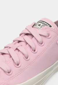 Rosa lærret sneakers med seks øyelet, flate rosa lisser, gummitåhette og hvit såle. Har et merke med "Converse All Star"-branding.