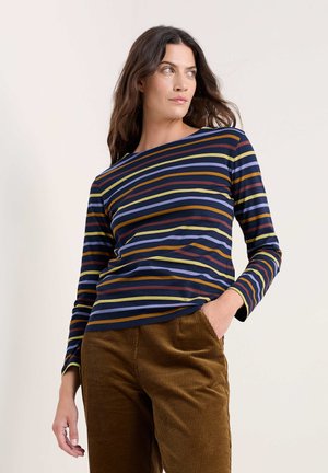Haut à manches longues bleu marine à rayures horizontales orange, jaune et bleu clair. Associe à un pantalon en velours côtelé marron.