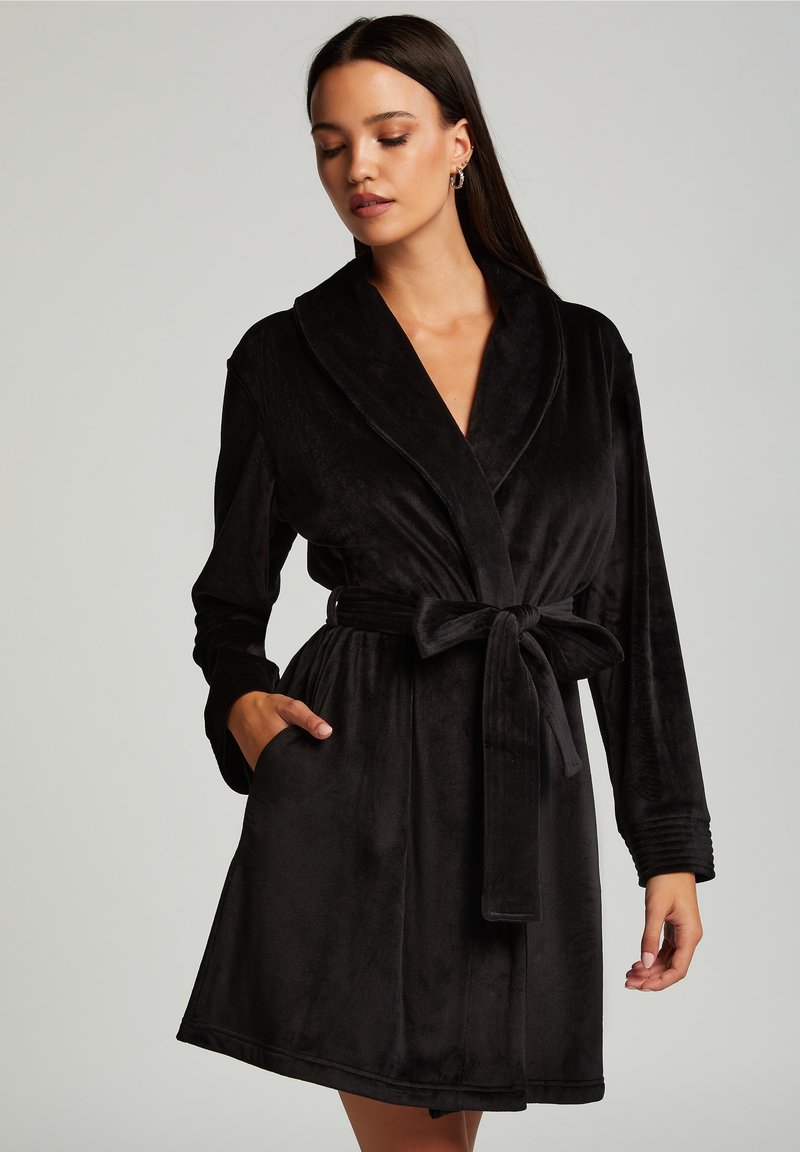 Svart sammetstol med sjalkrage, bältesmidja och långa ärmar. Har en mjuk textur och sidfickor. Enkelt och elegant design.