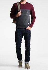 Felpa a blocchi di colore nero e bordeaux con maniche risvoltate, abbinata a jeans in denim scuro e sneakers verde oliva.
