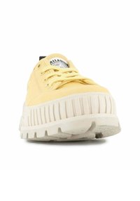 Zapatilla de lona amarilla con una suela de goma texturizada blanca, diseño de cordones y una etiqueta negra en la lengüeta con el logotipo de la marca.