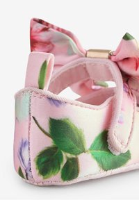 Różowe buciki wykonane z tkaniny, ozdobione kwiatowym wzorem z zielonymi liśćmi, miękką fakturą i kokardką z tyłu. Posiadają zapięcie na rzep.