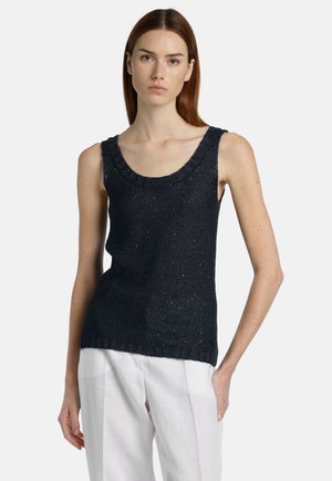 Top sin mangas de punto en color navy con escote redondeado, que presenta un acabado texturizado y sutiles destellos metálicos. Combinado con pantalones de lino blancos.