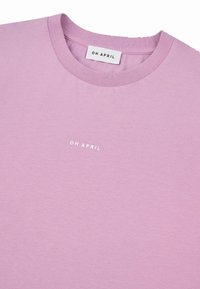 Gaiši rozā T-krekls ar apaļu kakla izgriezumu, no kokvilnas materiāla, ar mazu baltu "OH APRIL" logotipu uz priekšpuses un ribotas kakla izgriezuma malas.