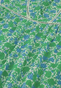 Bloemenjurk met een groen en blauw patroon op een witte achtergrond, met een gestructureerde afwerking en een delicate kanten rand langs de halslijn.