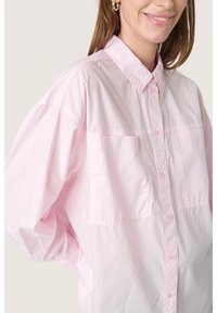 Camicia button-up rosa chiaro in cotone, con colletto, due tasche frontali e vestibilità oversize con maniche arricciate.
