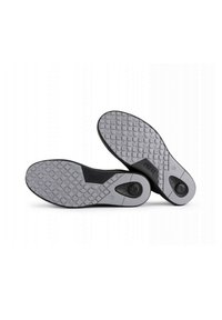 Suole di scarpe in gomma grigia con motivi testurizzati e accenti neri, dotate di punti di presa circolari e di un logo discreto sul lato.