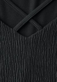 Černá tkanina s texturovaným povrchem, která má horizontální žebrování a hladké části. Design zahrnuje propletené ploché popruhy.