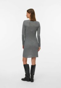 Siva rebrasto pleteno oblačilo z dolgimi rokavi, dolžina do kolen in rahlo poškodovanje ob robu. V kombinaciji z črnimi usnjenimi škornji do kolen.