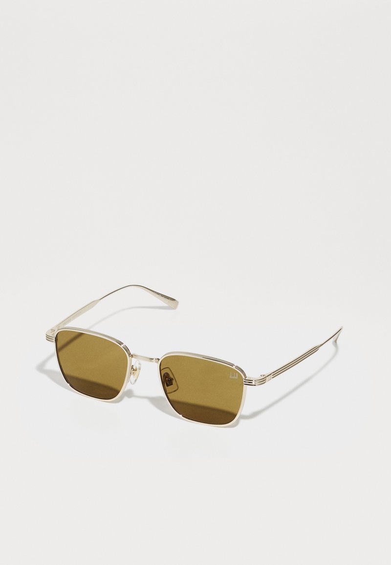 Lunettes de soleil en métal doré avec des verres carrés et une teinte brune. Le design élégant présente des branches fines et des accents matériels minimaux.