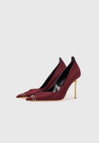 Burgundijas krāsas auduma augstpapēžu kurpes ar pirkstiem, kas norādīti, ar zelta akcentu pirkstos un metāliskām stiletto papēžiem. Gluda tekstūra.