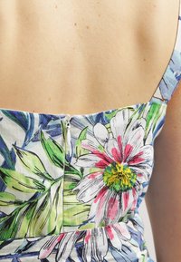 Robe en coton floral avec de vives marguerites roses et jaunes sur un fond bleu-vert. Le dos présente une fermeture zippée discrète.