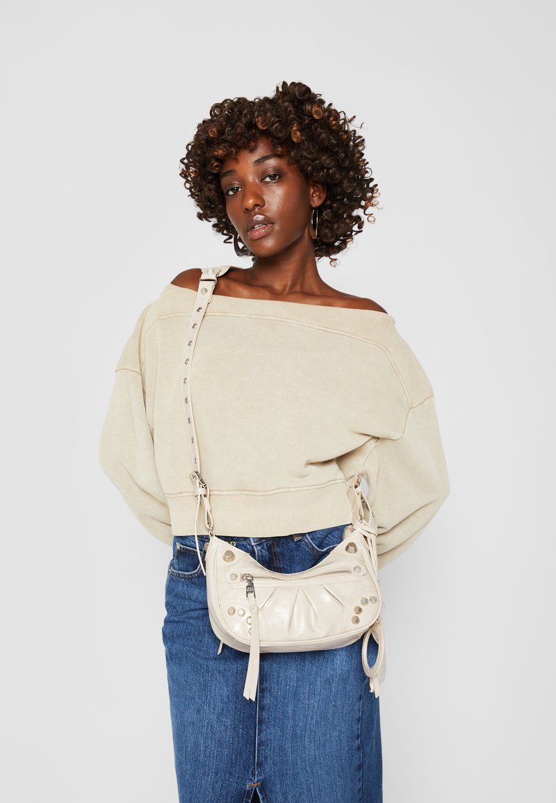 Suéter beige sin hombros, falda de mezclilla azul y un pequeño bolso cruzado de cuero crema con detalles de tachuelas y borlas.
