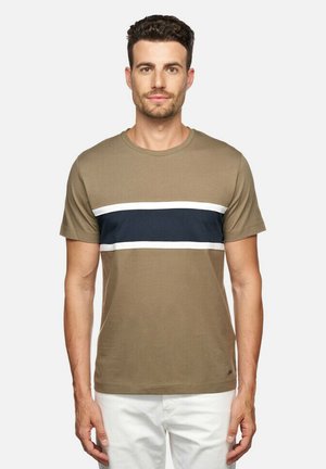 T-shirt vert olive à manches courtes avec des rayures horizontales navy et blanches, encolure arrondie et tissu en coton lisse, porté avec un pantalon blanc.