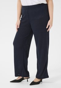 Pantalones de pierna ancha en color navy con textura acanalada, cinturilla elástica y tejido ligero, combinados con zapatos negros de punta afilada.