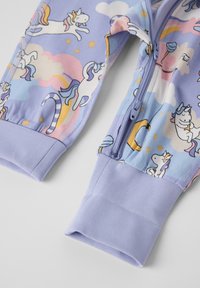 Violetin yöasu, jossa on leikkisä yksisarvinen kuvasto vaalealla taustalla, vetoketjukiinnitys ja pehmeät ribbihihnat.